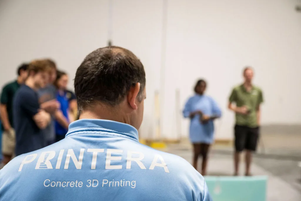 Back view of Printera’s CEO wearing a company shirt while observing a 3D concrete printing education presentation at the Printera facility.